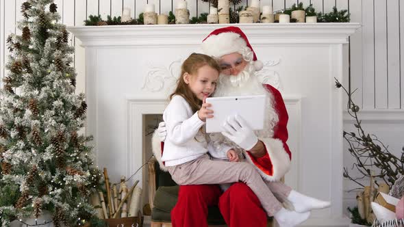 Happy Little Girl Showing Surprised Santa Presents on Tablet