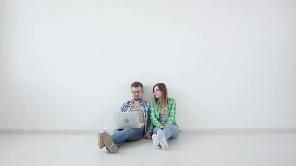 Young Happy Couple Is Sitting in an Empty Room and Planning To Arrange Furniture in a New House