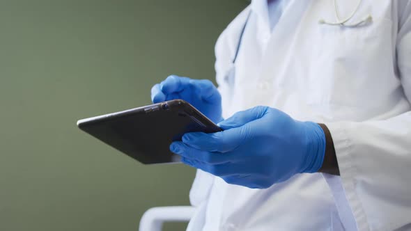 African american senior male doctor wearing face mask using digital tablet at hospital