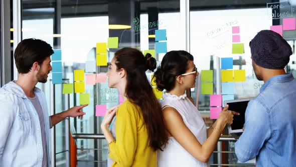 Executives discussing over sticky notes on glass wall