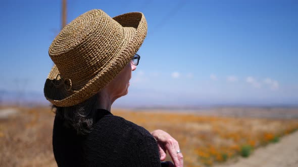 An old woman in summer heat pointing down a dirt road hitchhiking in an empty field of orange Califo