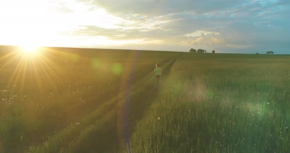 Sporty Child Runs Through a Green Wheat Field in Summer Rain. Evening Sport Training Exercises at