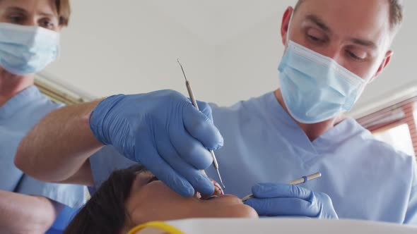 Caucasian male dentist with face mask examining teeth of female patient at modern dental clinic