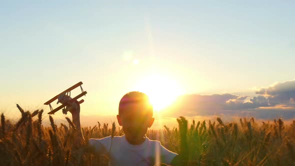 A Happy Child Is Running Across a Wheat Field During Sunset, Holding a Toy Plane. The Boy Shows the