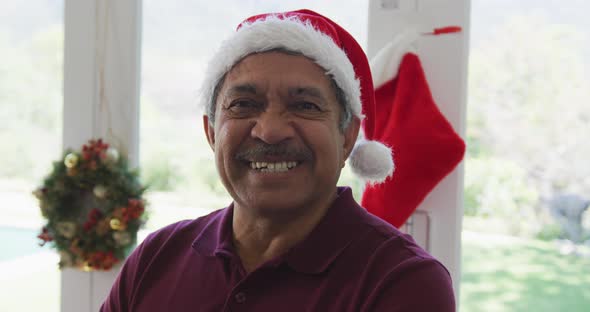 Portrait of cheerful senior man in santa hat at decorated home during christmas