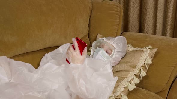 Teenager Girl in Protective Costume and Mask Looking Smartphone on Couch