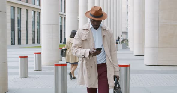 Confident African Businessman Walking with Leather Bag and Mobile Phone Outdoors