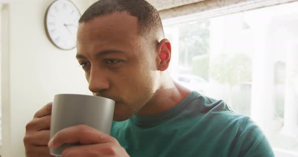 Portrait of thoughtful biracial man in kitchen drinking coffee