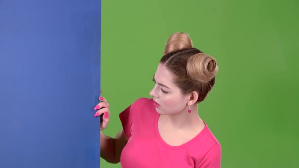 Teenager Peeks Out From Behind a Blue Board and Shows a Thumbs Down. Green Screen. Slow Motion