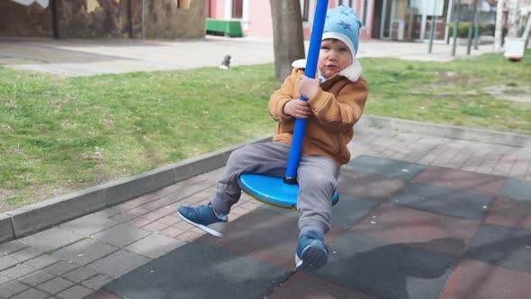 A Boy on a Playground in an Autumn Park Rides on a Swing in Cloudy Weather