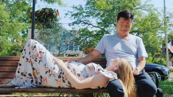 Asian Man with a Pregnant Wife are Resting in a Park on a Bench