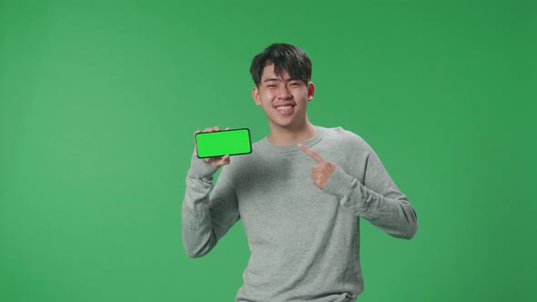 Asian Man Holding And Pointing Mobile Phone With Green Screen On Green Screen Background