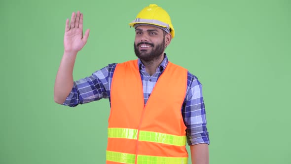 Happy Young Overweight Bearded Indian Man Construction Worker Waving Hand