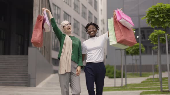 Portrait of Two Diverse Young Women African and Muslim Holding Colorful Shopping Bags