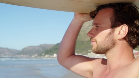 Young man carrying surfboard on head at beach