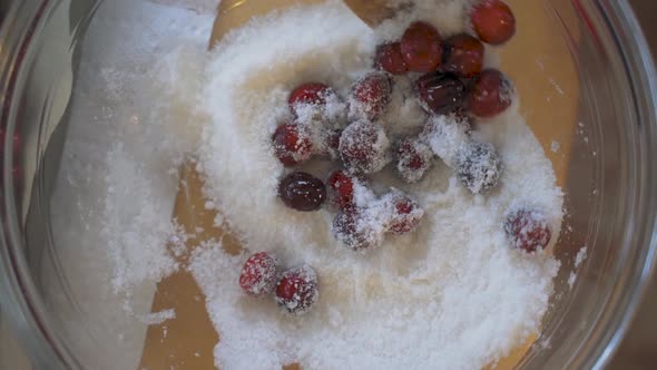 Slow motion overhead wooden spoon mixing and stirring fresh red cranberries and white sugar in clear