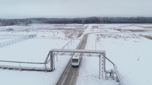 A White Bus Passes Under Pipes on a Snowy Road