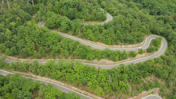 An RV driving down a steep mountain road with numerous hairpin bends. Wide angle aerial approach