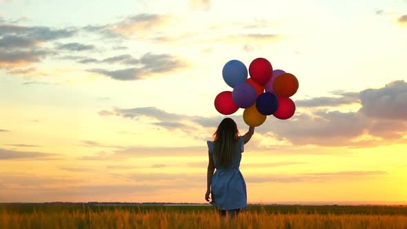 Happy Woman with Balloons Running in the Wheat Field at Sunset