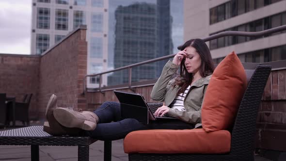 View of woman relaxing on roof top typing on laptop running fingers through hair.