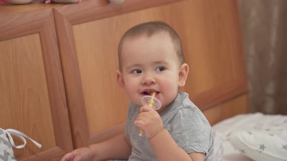 Newborn girl 12-17 months brushing teeth with a toothbrush sitting on the bed