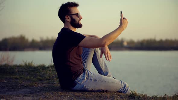 Male Sitting With Phone On Beach. Freelancer Internet Online Meeting Webinar. Video Call.