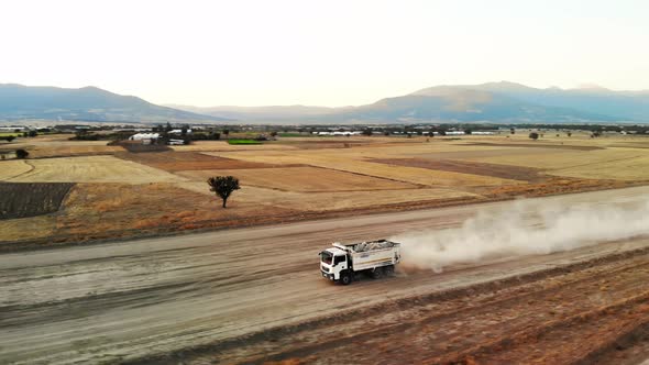 Aerial Footage Large White Truck with Truck Loaded with Rocks is Driving Down Gravel Road with Dust