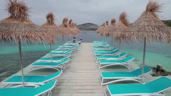 Aerial View of Empty Sunbeds Under Thatched Umbrellas on a Pier in Turquoise Sea