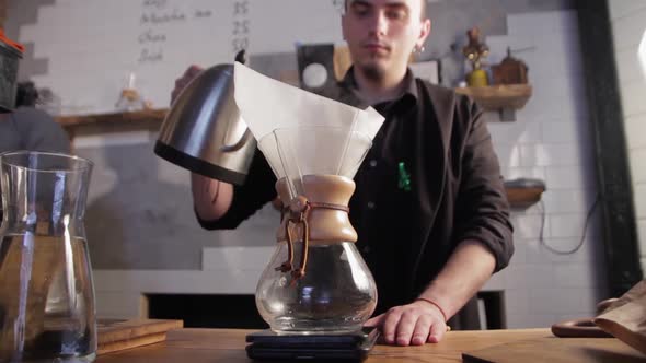 Barista pouring hot water into filter with coffee. Brewing coffee in a chemex