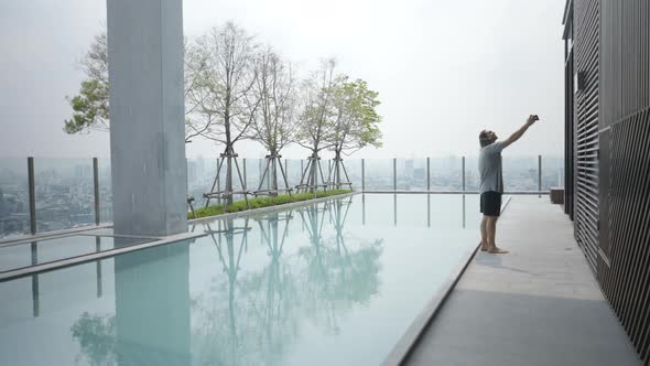 Tourist Standing By The Poolside While Taking Selfie