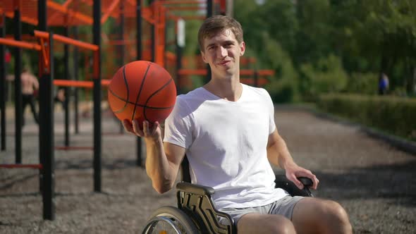 Portrait of Positive Man in Wheelchair Holding Basketball Ball Smiling Looking at Camera