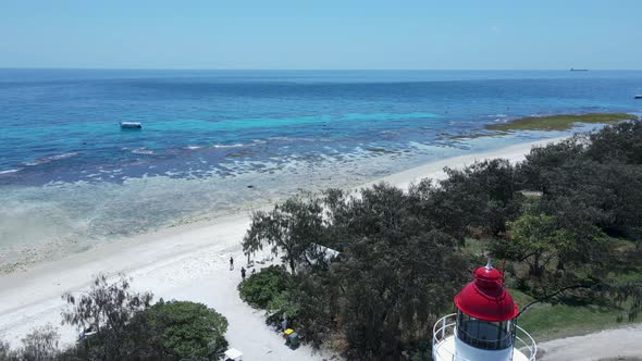 Unique lighthouse looking over a tropical reef surrounded by shades of blue water. Moving drone view