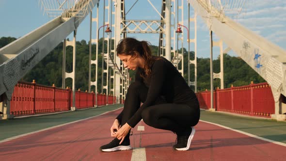 Young Athlete Woman Tying Running Shoes with Earphones on the Ground. Female Runner Ties Sneakers