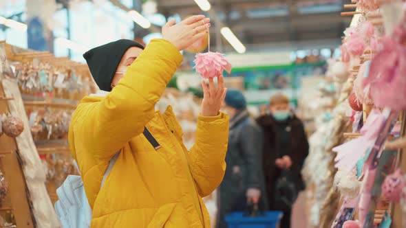 Woman in Yellow Winter Jacket Choosing Christmas Ornament on Christmas Market in Shopping Mall