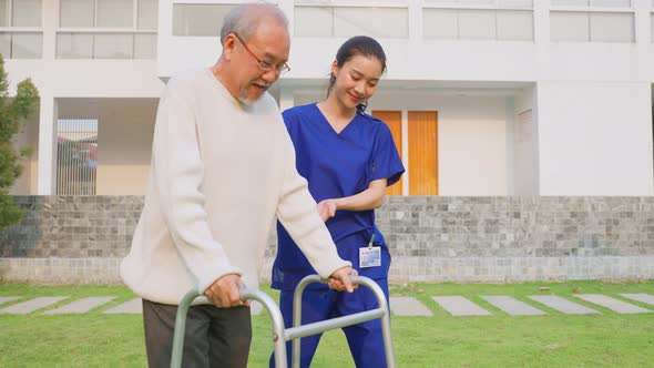Asian young caregiver nurse support senior older male walking in public park at nursing home.