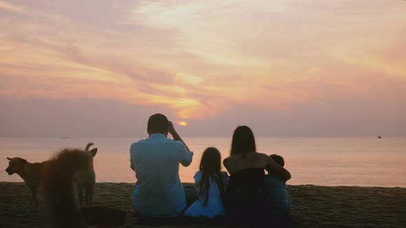 Beautiful Back View Shot of Happy Family Sit Together Watching Amazing Sunset on Epic Sea Beach