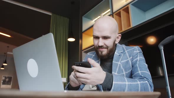 Business Man in a Suit Sitting in a Cafe Works at a Laptop and Surfs the Phone