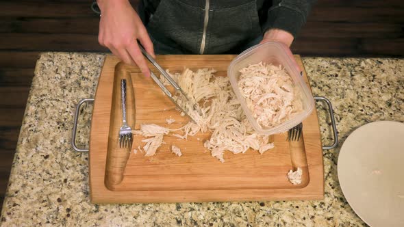 Caucasian male putting skinless shredded chicken breast into plastic food containers, top-down