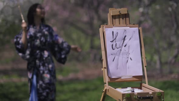 Canvas with Painting on Easel in Sunlight with Blurred Slim Asian Woman in Kimono Dancing with White