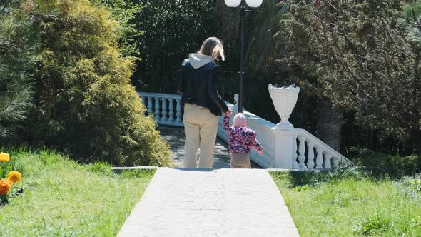 Mom and Daughter in Spring Go Down Stone Steps in Park and Go to Look at Flowers