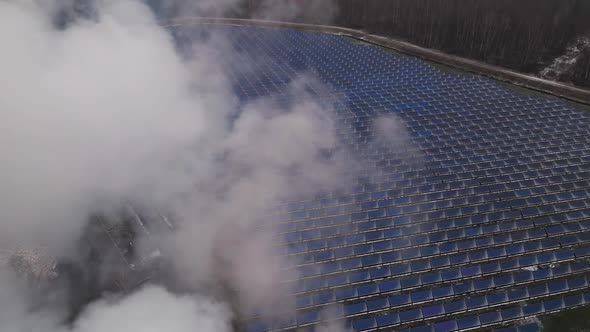 Descending Aerial View Through Smoke Over Field of Solar Battery Cells in Winter