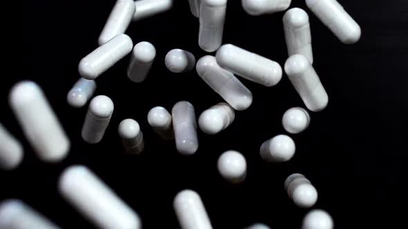 White capsules of vitamins fly up and hover in the air in slow motion against a black background