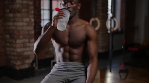 A Shirtless Africanamerican Handsome Man Training in the Gym  Drinking Water From the Plastic Bottle