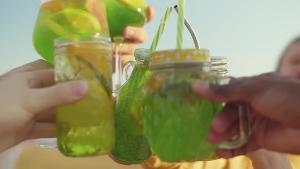 Hands Holding Glasses with Cocktails and Clinking Glasses Against the Background of a Sunny Sky