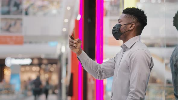 Young Businessman in Protective Mask Holding Phone Using Mobile Application for Remote Communication