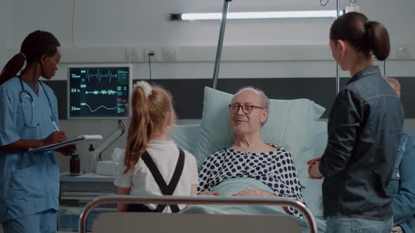 Aged Patient Talking to Little Girl in Hospital Ward Bed