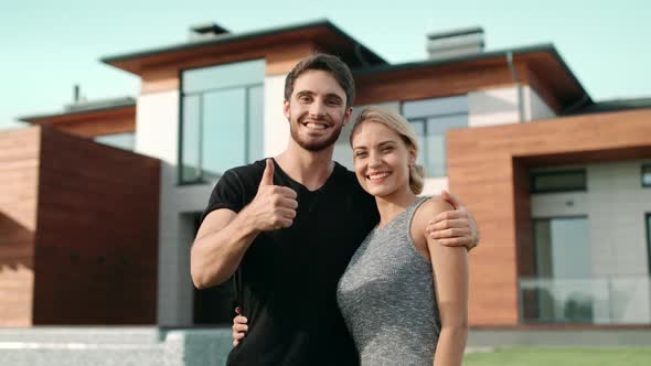 Happy Couple Making Thumbs Up Gesture Near Luxury House