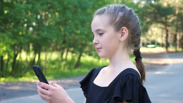 Schoolgirl Types on Phone Standing on Forest Road Closeup