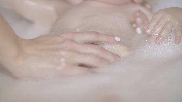 Mother's Hand Touching and Washing Her Newborn Baby Covered White Foam in Bath