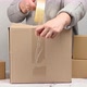woman in a gray sweater holds a roll of duct tape and packs brown cardboard boxes  - VideoHive Item for Sale
